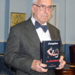 elderly man with glasses wearing a brown jacket and blue polka dotted bow tie holding a book titled couples in combat - baggage