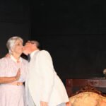 Gray haired woman wearing a pink dress smiling as a man wearing a white suit kisses her cheek- driving miss daisy