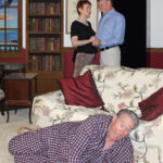 man wearing plaid pajamas lying on the floor in front of a sofa looking surprised, with a man and woman standing behind the couch holding hands and looking at one another-jack of diamonds