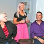 angry woman in black jacket staring and man in purple shirt - smiling woman with pink hair wearing a black shirt and pink skirt holding two glasses- men are dogs