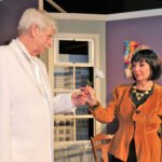 elderly man in a white suit handing a white rose to a woman with black hair wearing an orange jacket - you should be so lucky