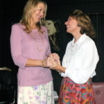 tall blond smiling woman wearing a lavender top with floral skirt looking dow and smiling woman wearing a floral skirt and white blouse-steel magnolias